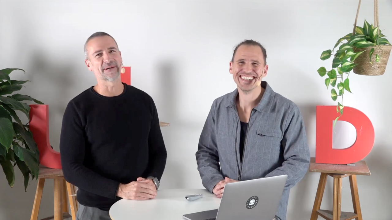 Two men sitting at a table with a laptop.