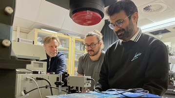 Tre män i ett laboratorium som tittar på något som ligger på ett bord.
