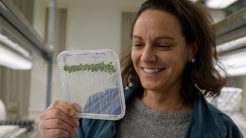 A woman holding up a plastic container with a plant inside of it.