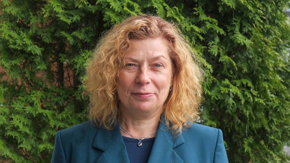 Portrait of a woman with blond curly hair, wearing a blue jacket.
