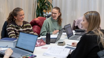 En grupp studenter sitter vid ett bord med bärbara datorer.