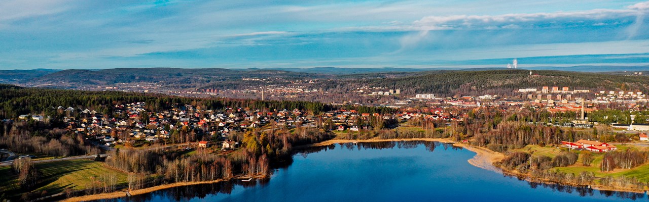 Helikoptervy över en sjö med bebyggelse i bakgrunden. Sjön och hilmen är blå