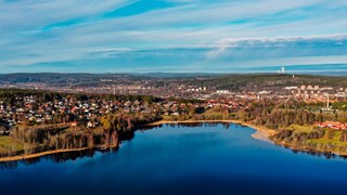 Helikoptervy över en sjö med bebyggelse i bakgrunden. Sjön och hilmen är blå