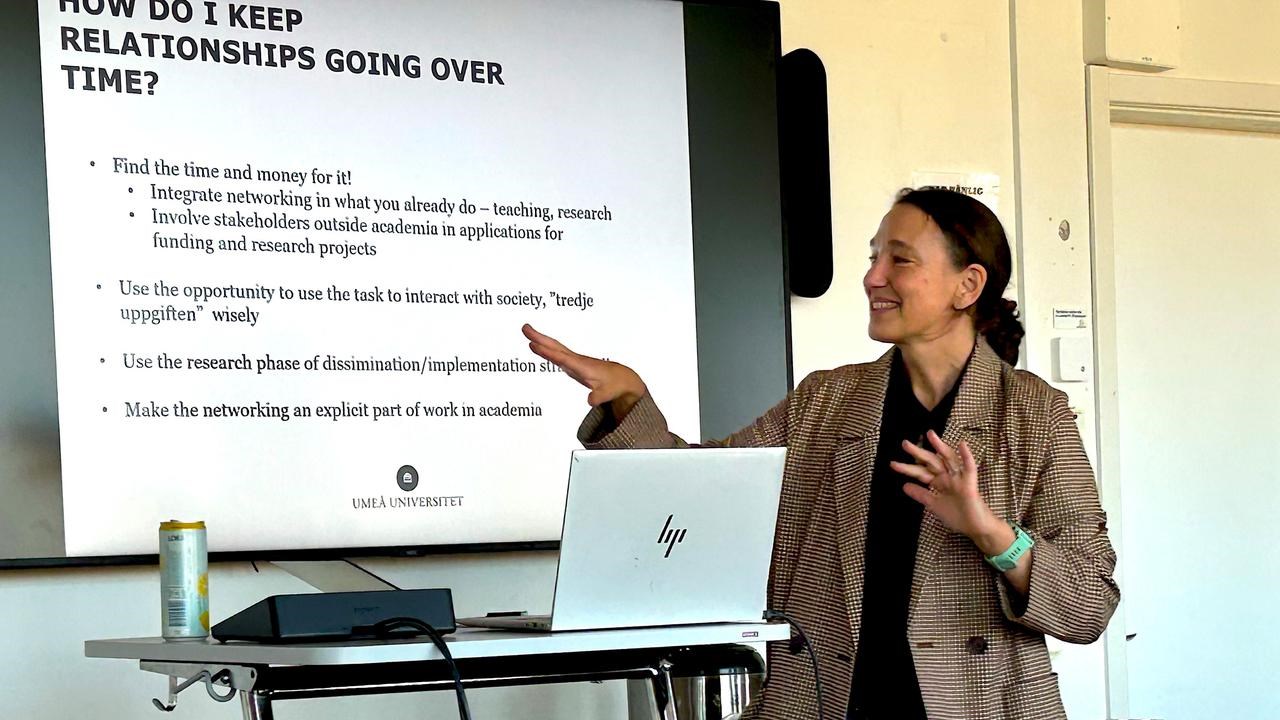 A woman standing in front of a screen, holding a presentation.