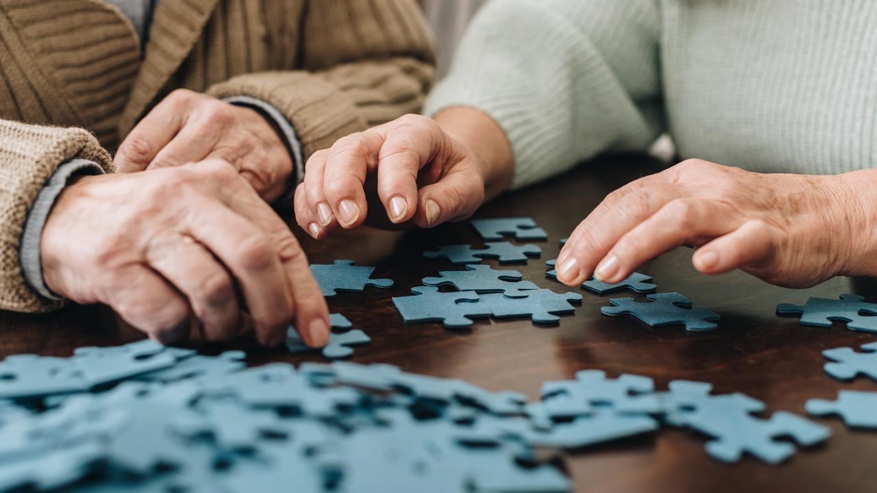 Två äldre personer lägger pussel tillsammans. Närbild på händer.