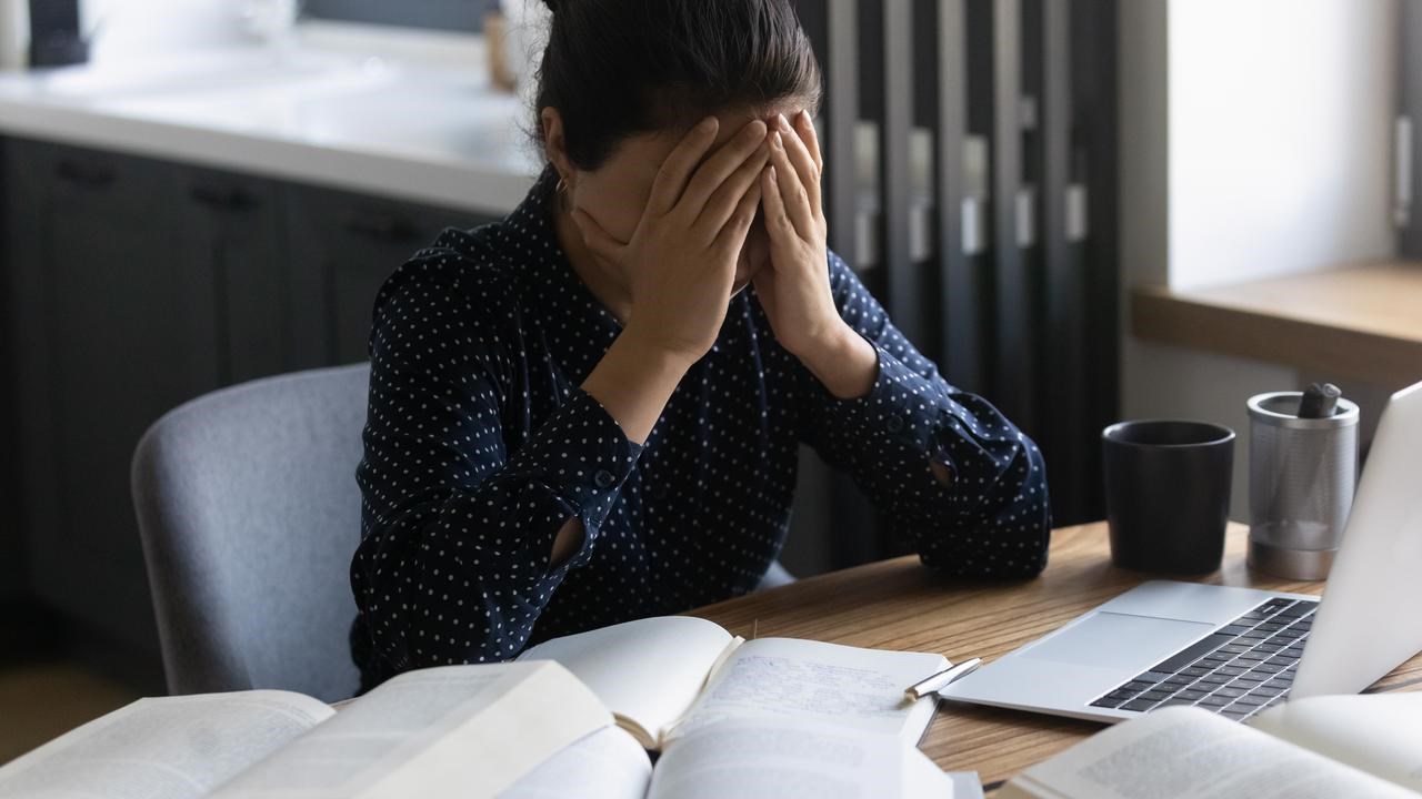 Kvinna sitter framför datorn och böcker med händerna framför ansiktet.