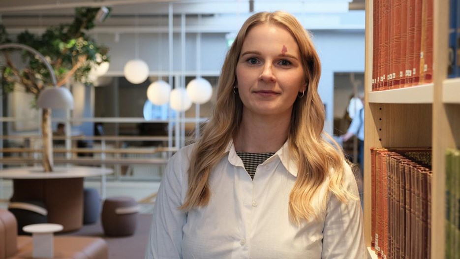 En kvinna står framför en bokhylla.
