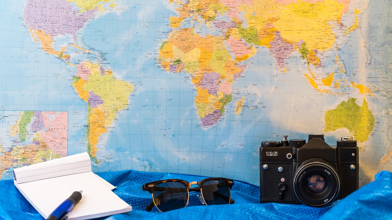 Bild på världskarta, anteckningsblock, solglasögon och kamera för att illustrera resa eller internationalisering.