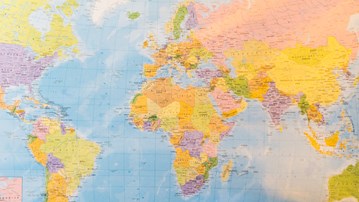 Bild på världskarta, anteckningsblock, solglasögon och kamera för att illustrera resa eller internationalisering.