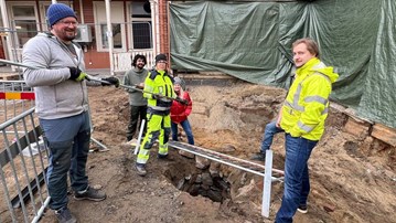 Foto av fem personer i varselkläder står runt en stenlagd gammal brunn på en byggarbetsplats.