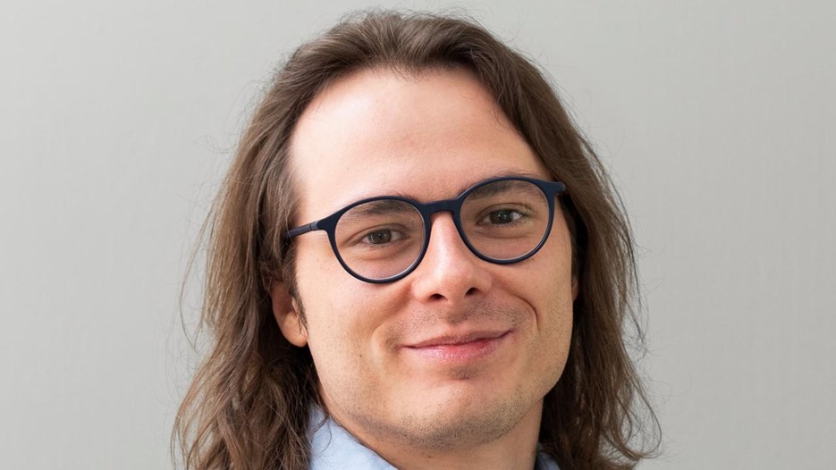 A man with long hair wearing glasses and a blue shirt.