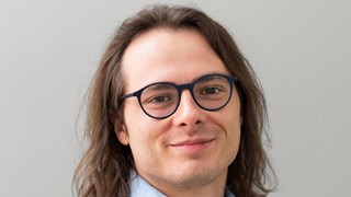 A man with long hair wearing glasses and a blue shirt. 