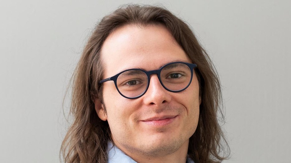 En man med långt hår, glasögon och en blå skjorta.