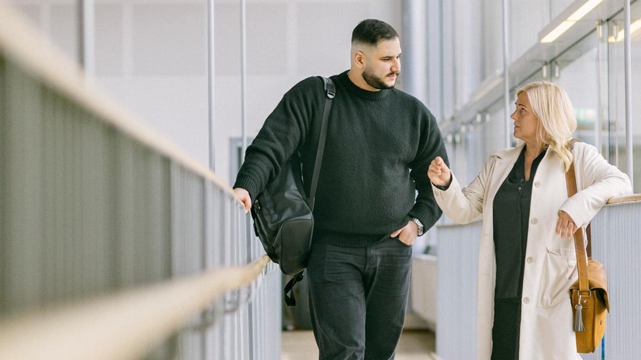 Två personer står på en loftgång inomhus och tittar talar med varandra