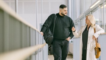 Två personer står på en loftgång inomhus och talar med varandra