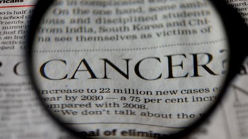 Närbild på ett förstoringsglas som visar ordet Cancer från en tidningstext