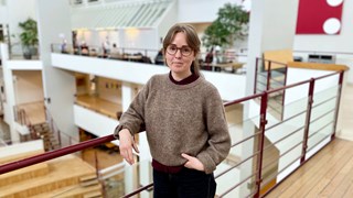 Kvinna står lutad mot ett räcke med en ljusgård i bakgrunden.