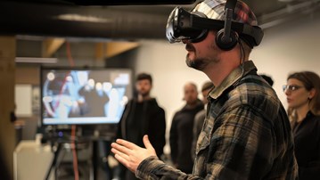 Man som står med ett par svarta VR-glasögon på sig.