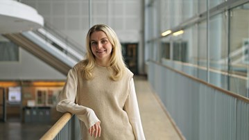 En kvinna i en beige tröja står på en balkong.