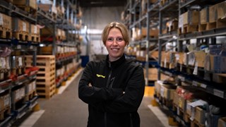 En kvinna som står i en lagerlokal med många hyllor.