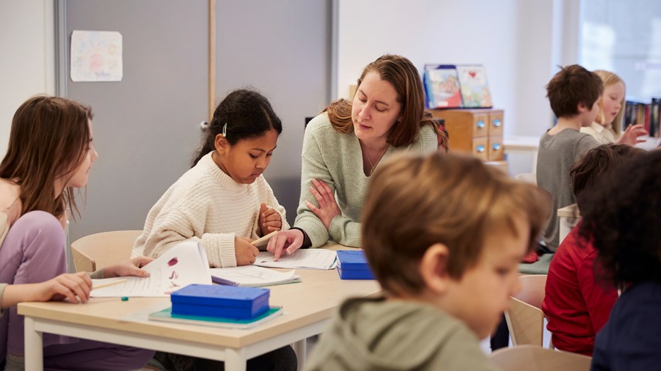 Lärare hjälper barn med uppgift, i klassrum.