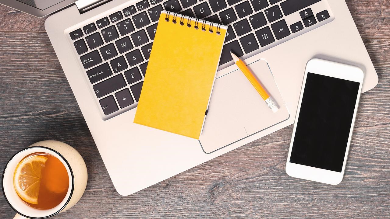 Dator, anteckningsblock, mobil och penna fotat uppifrån på ett bord.