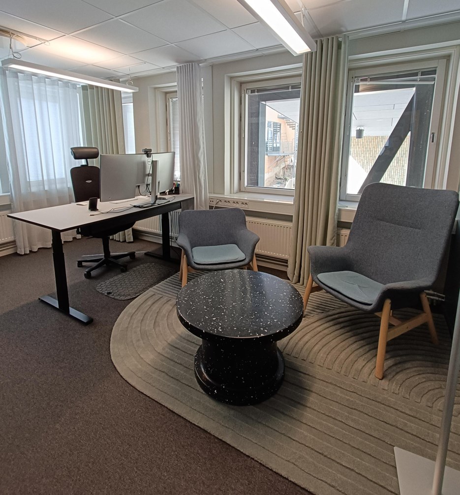 Open office with a desk and two comfortable chairs. The room is light with many windows.