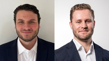 Två kostymklädda män ler mot kameran.