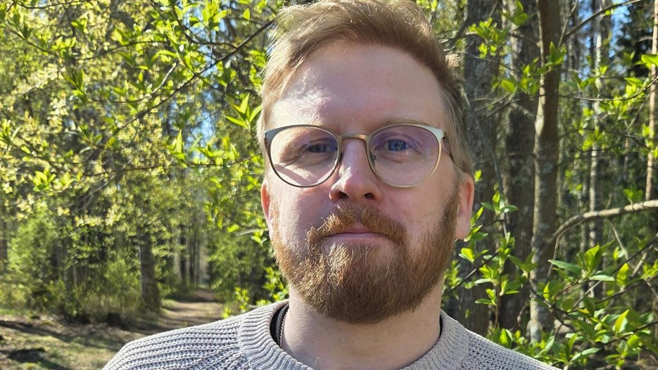 En man med skägg och glasögon står framför en skog.