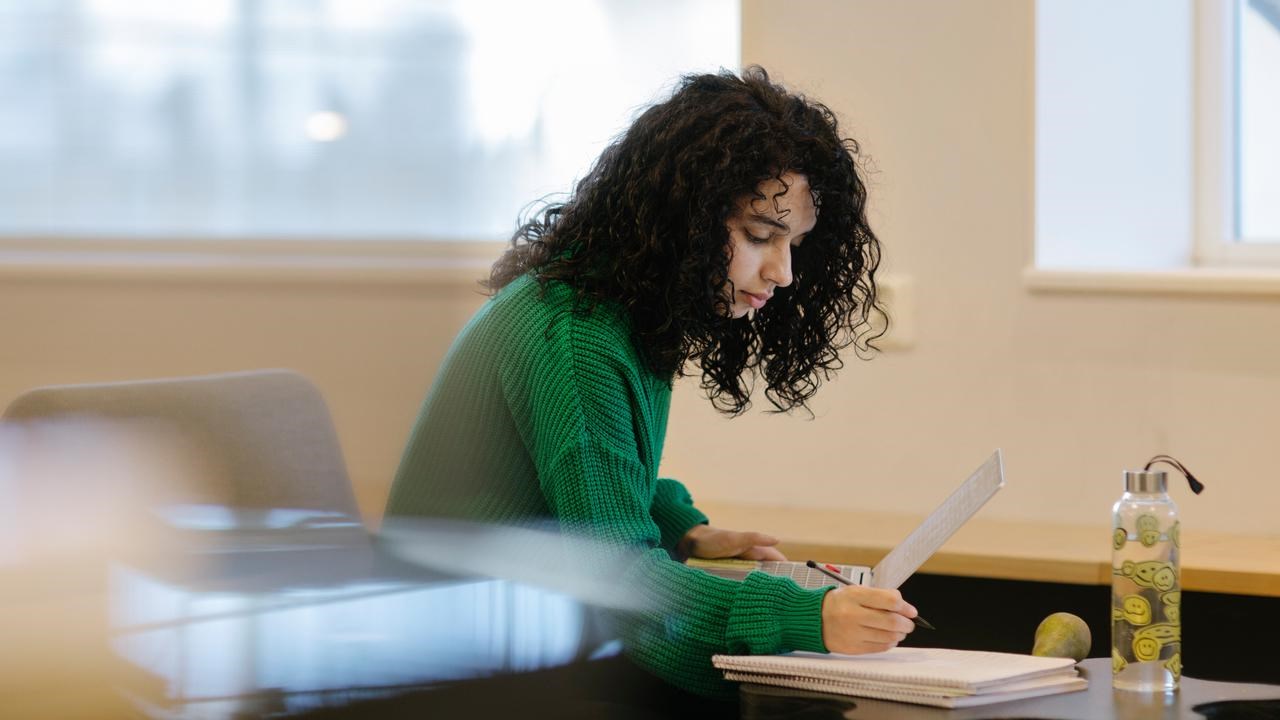 Studenten Sarah pluggar med dator och anteckningsblock.