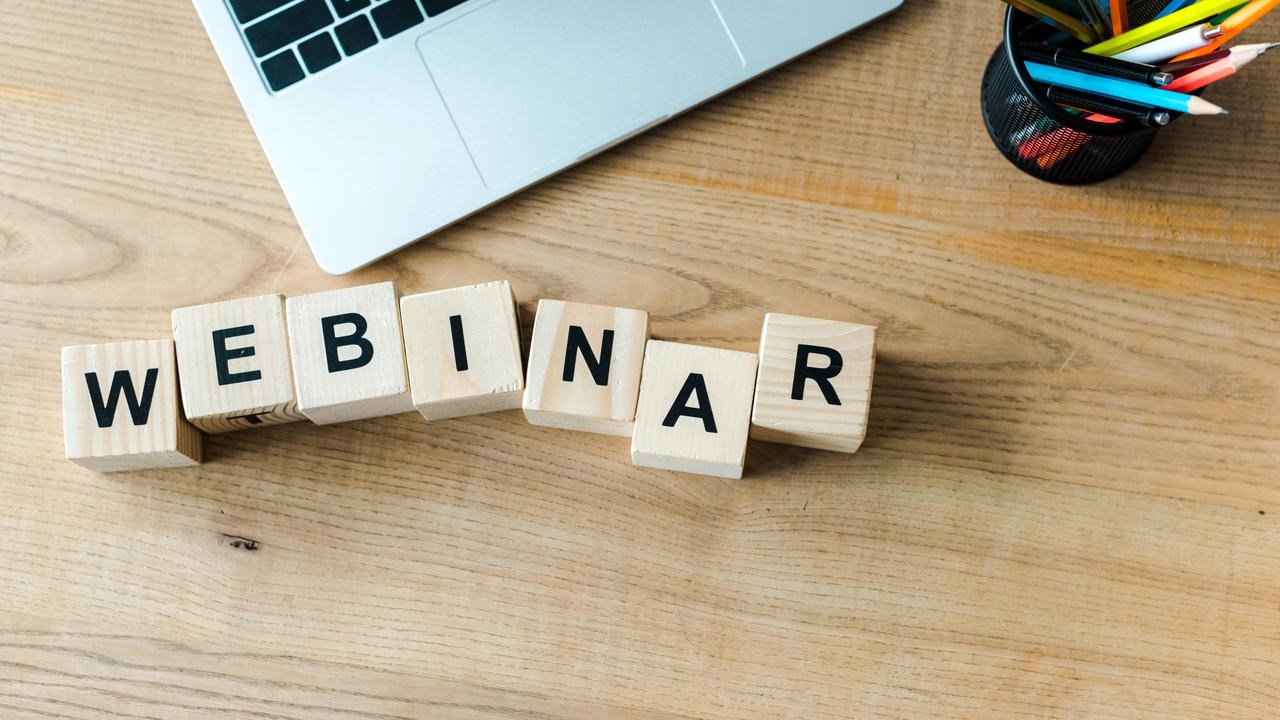 Träklossar på skrivbord bredvid laptop som bildar ordet webinar.