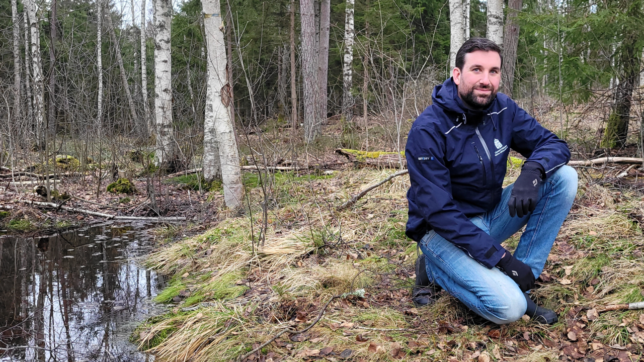 Joel Avenius stående med skogsmark och en å i bakgrunden