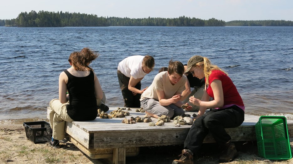 Bild på studenter som undersöker stenar vid en sjö