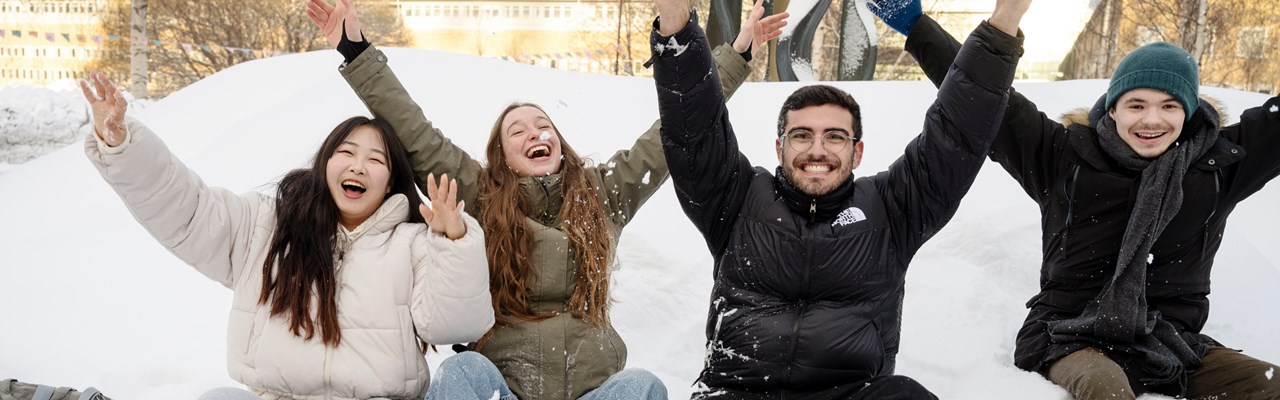 Leende studenter på en snöhög med armarna i luften