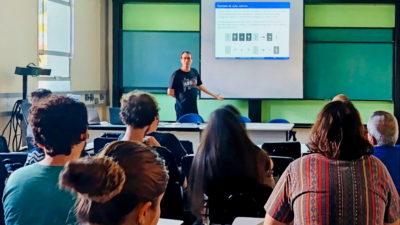 Ricardo föreläser framför elever och sträcker ut handen mot powerpointen i bakgrunden