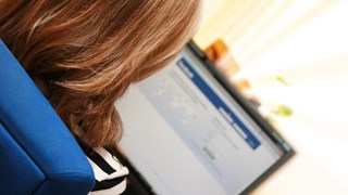 Bild på en person med långt hår avbildad bakifrån när hen surfar på Facebook på en bärbar dator.