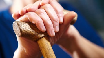 Äldre kvinnas hand på käpp.
