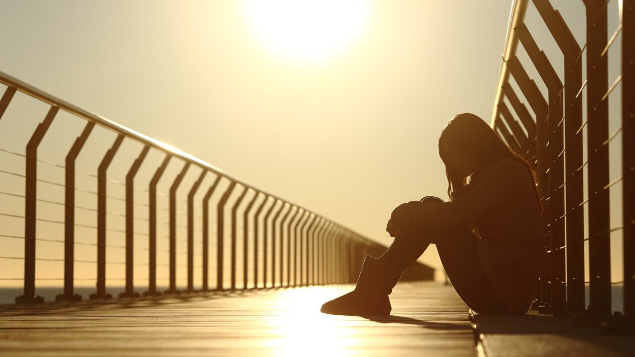 Sad teenager girl depressed sitting in a bridge at sunset