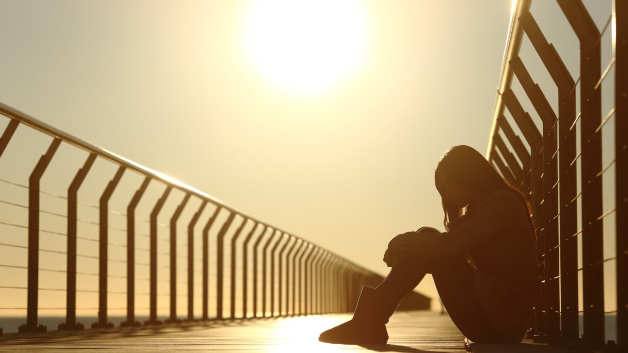 Sad teenager girl depressed sitting in a bridge at sunset