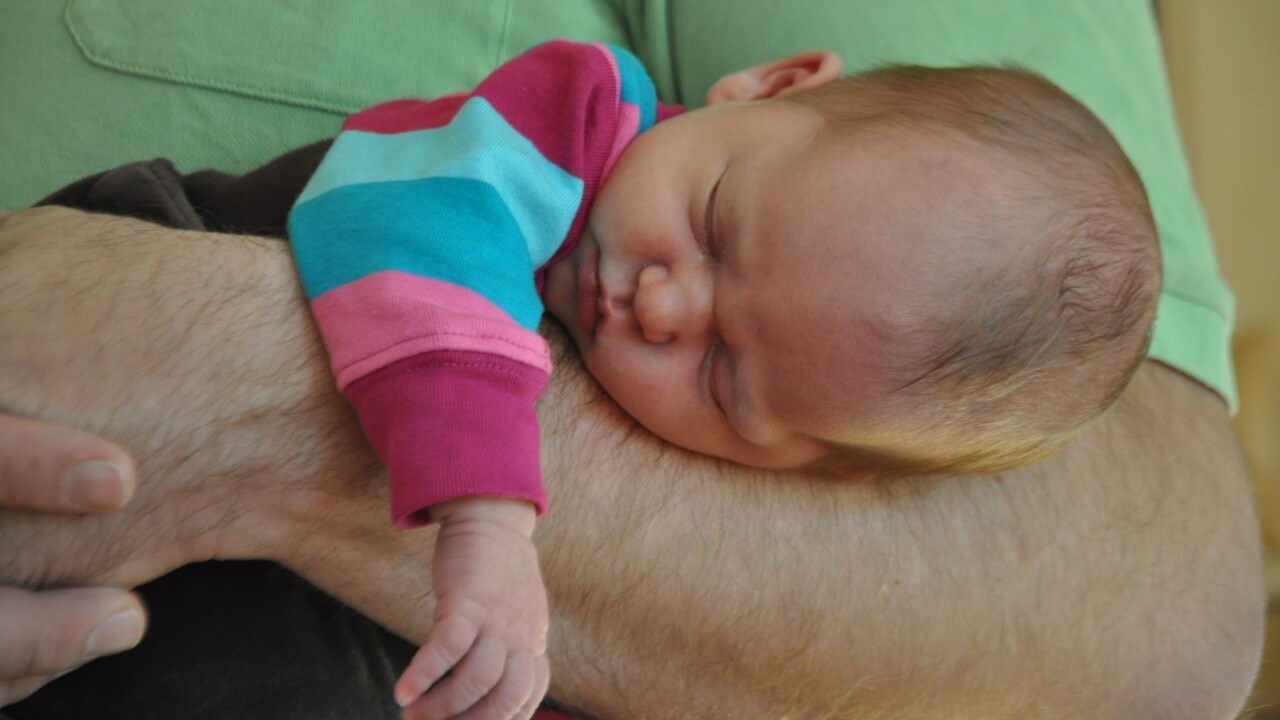 Pappa med sovande baby på armen.