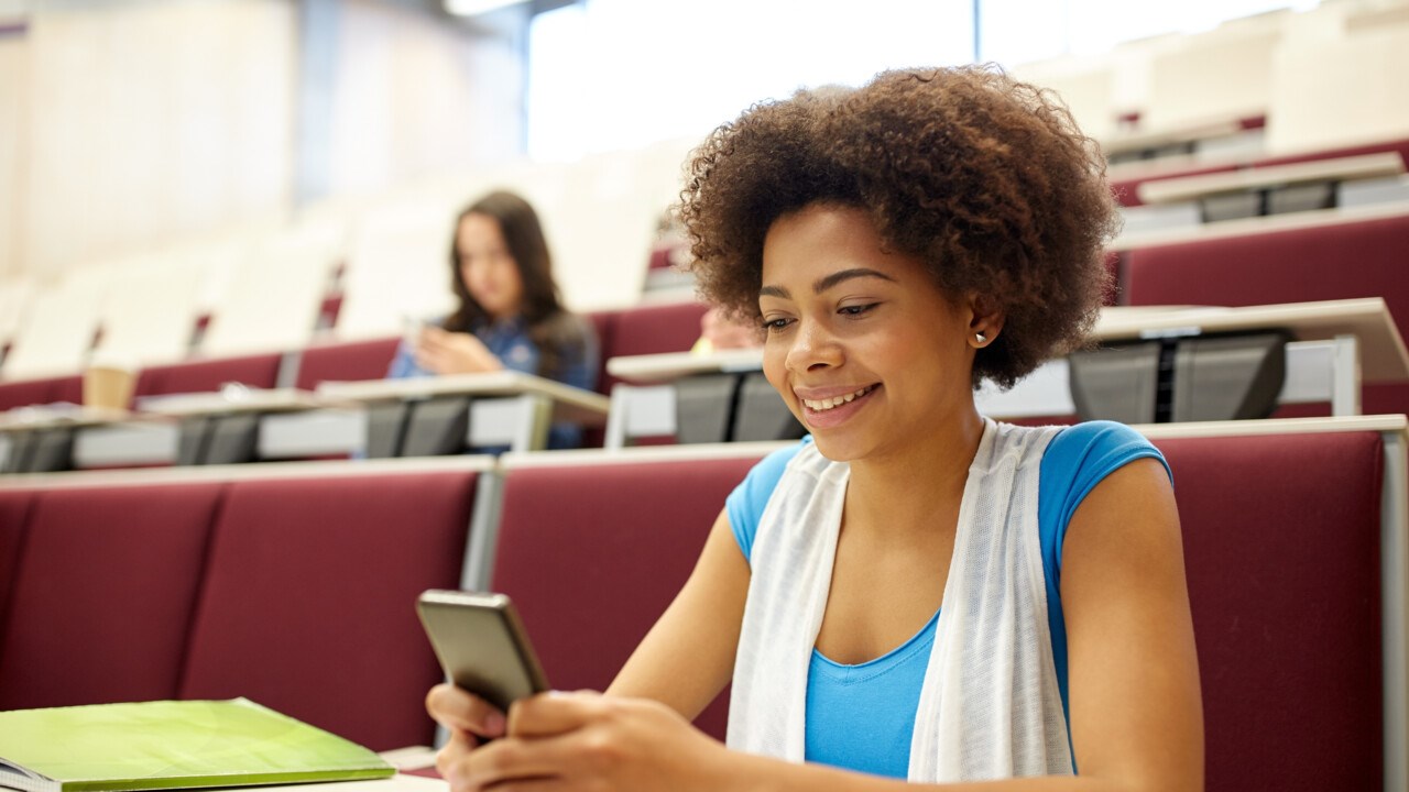 Smiling student in a hall looking at her mobile phone.