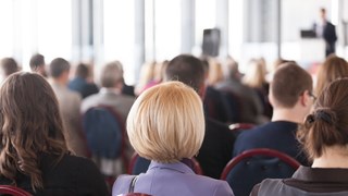 Photo of a audience sitting down and looking at a male speaker