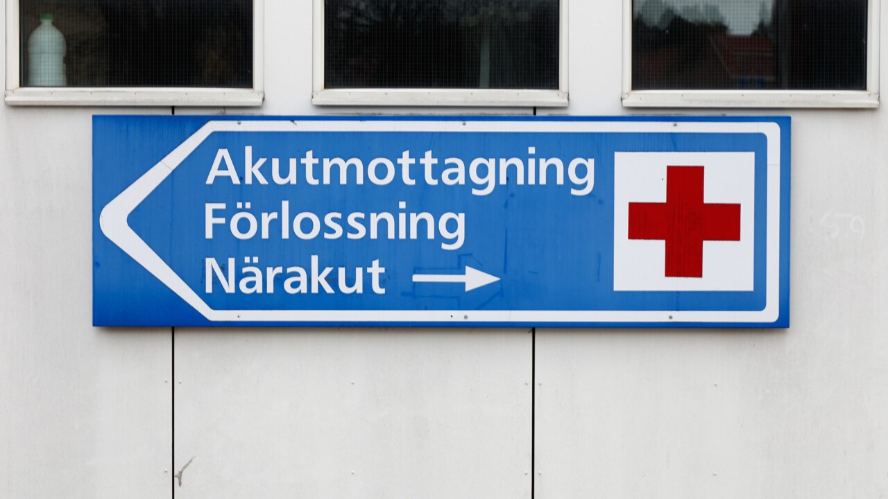 Vägvisande skylt med rött kors vid sjukhus med Akutmottagning, förlossning och närakut.