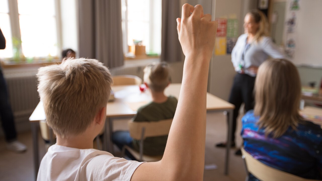 Mellanstadiebarn i klassrum. Pojke räcker upp handen.