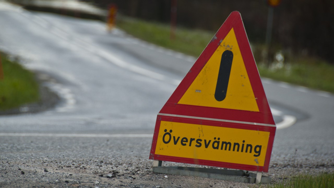 Bild på varningsskylt med texten Översvämning som står på en väg.
