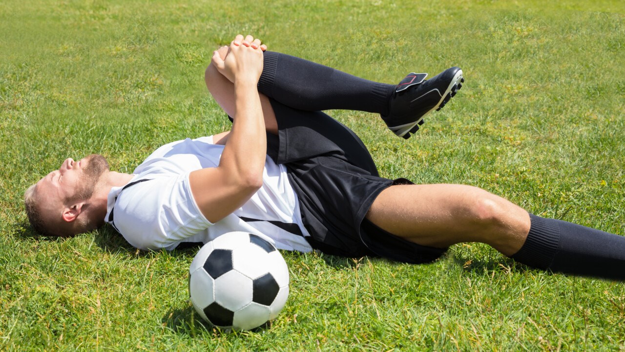 Manlig fotbollsspelare ligger på marken och tar sig för knät.
