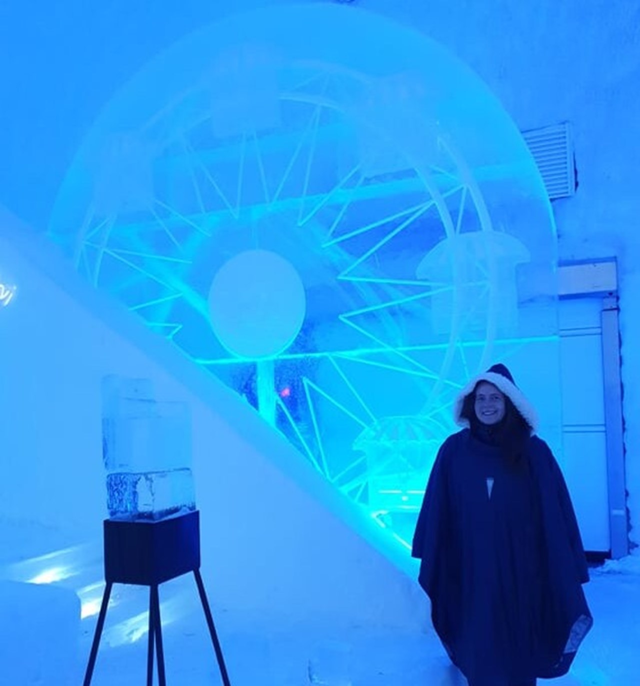 Moa Mattson, Doktorand vid Institutionen för tillämpad fysik och elektronik, Umeå Universitet står iklädd en lång mörk poncho med pälskrage vid en isformation 'Pariserhjul' inne i ishotellet i Jukkasjärvi.