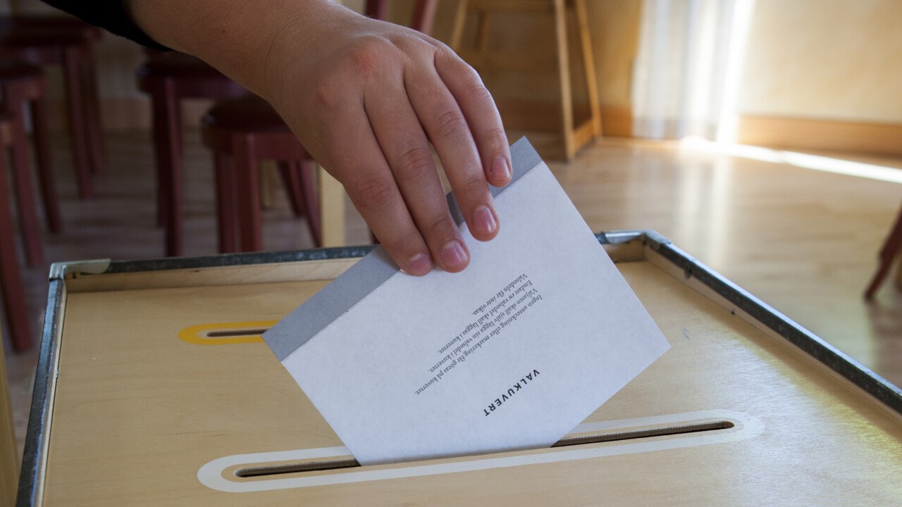 Hand som lägger ett valkuvert i valurnan i en röstlokal.