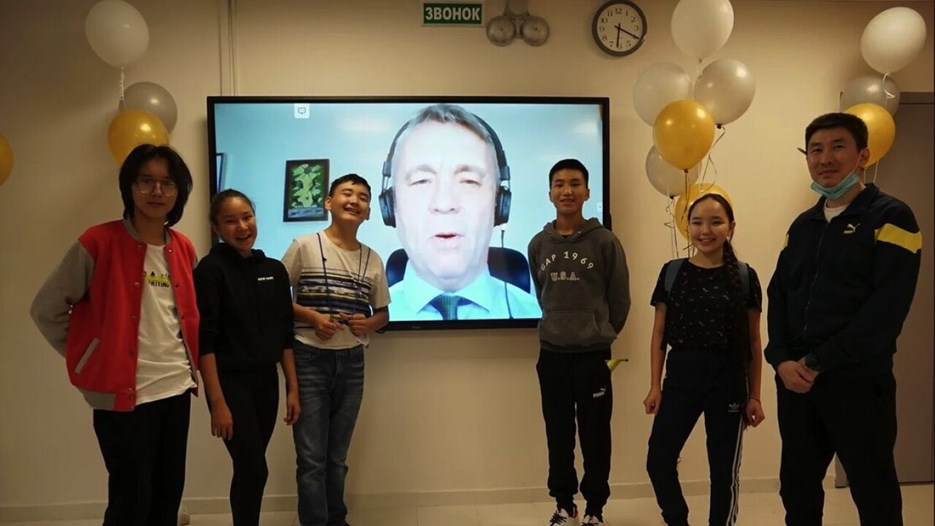 Students stand on either side of a large screen smiling at the camera while Peter Sköld's wishes can be seen on the screen in the background