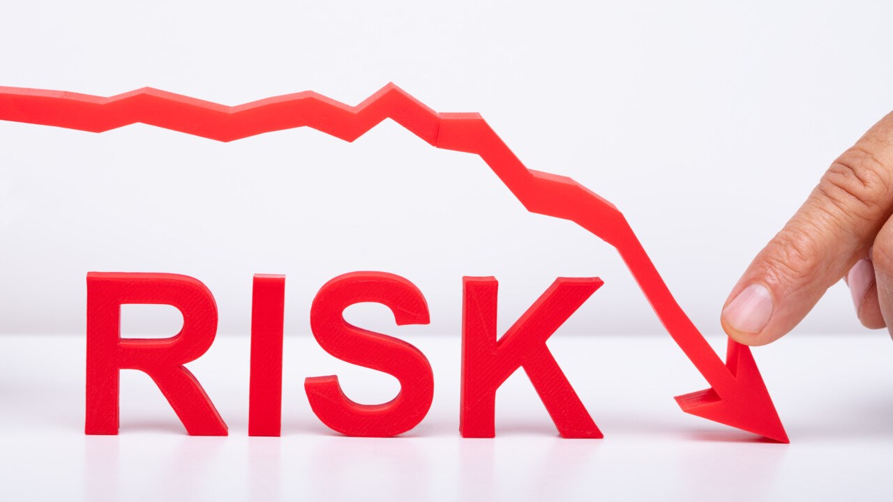 Finger som håller på en nedåtgående pil med ordet Risk under. Ska illustrera att minska risken.